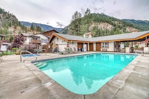 A pool area with a clear blue pool, lounge chairs, and a building with a sloped roof.