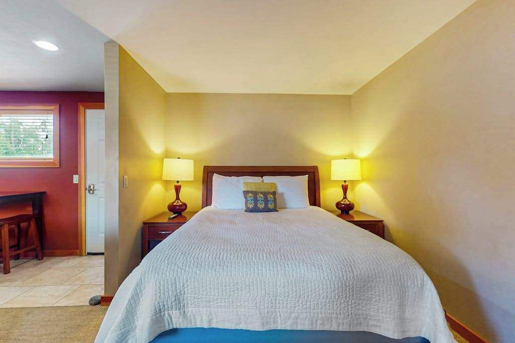 A hotel room with a large bed, two bedside lamps, a wooden headboard, and a small desk with a chair.