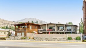 A two-story building with a balcony on the upper level, a stone facade, and a view of mountains in the background. - Lovely Studio Mountainview - Patio - Pool (Chelan)