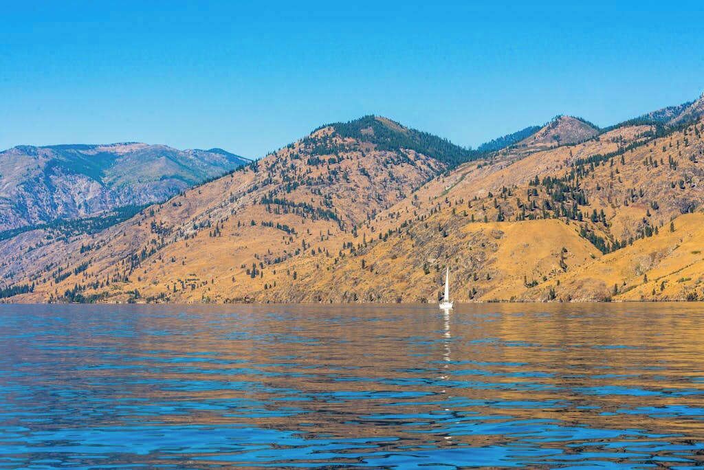 Un lago con un velero, rodeado de montañas.