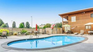 A swimming pool with lounge chairs and umbrellas, surrounded by a wooden building with a balcony. - Lovely Studio Mountainview - Patio - Pool (Chelan)