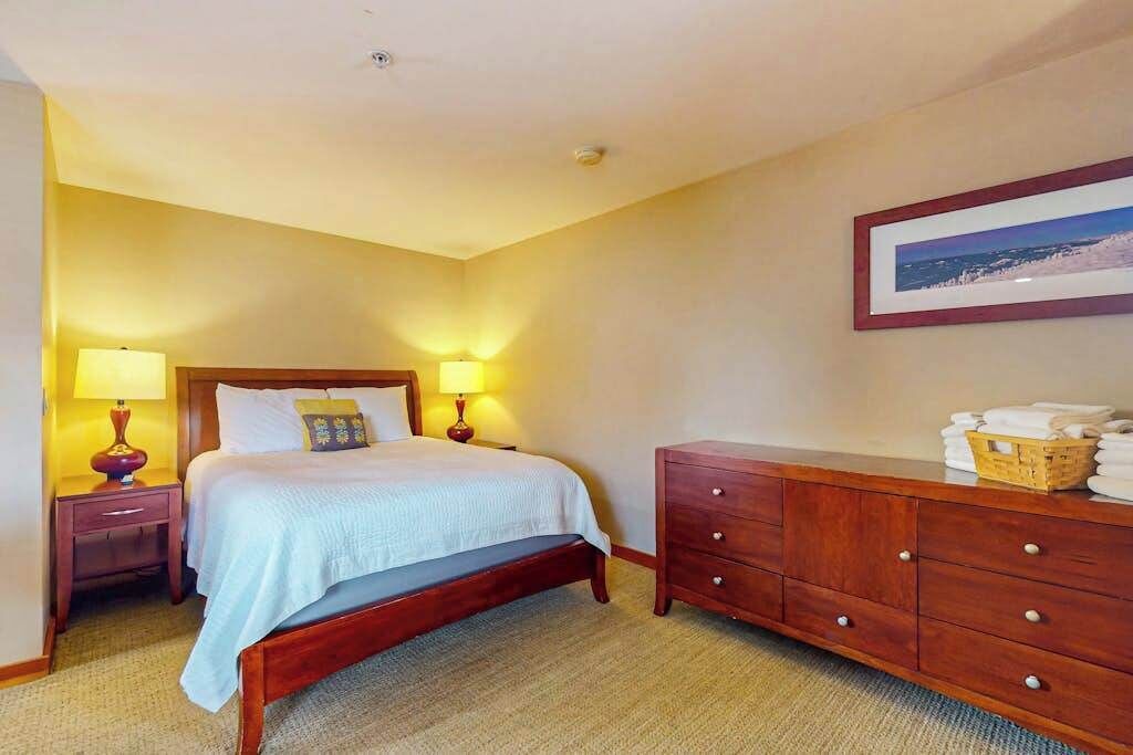 Une chambre d’hôtel avec un lit, des lampes de chevet, une commode en bois et un tableau encadré au mur.