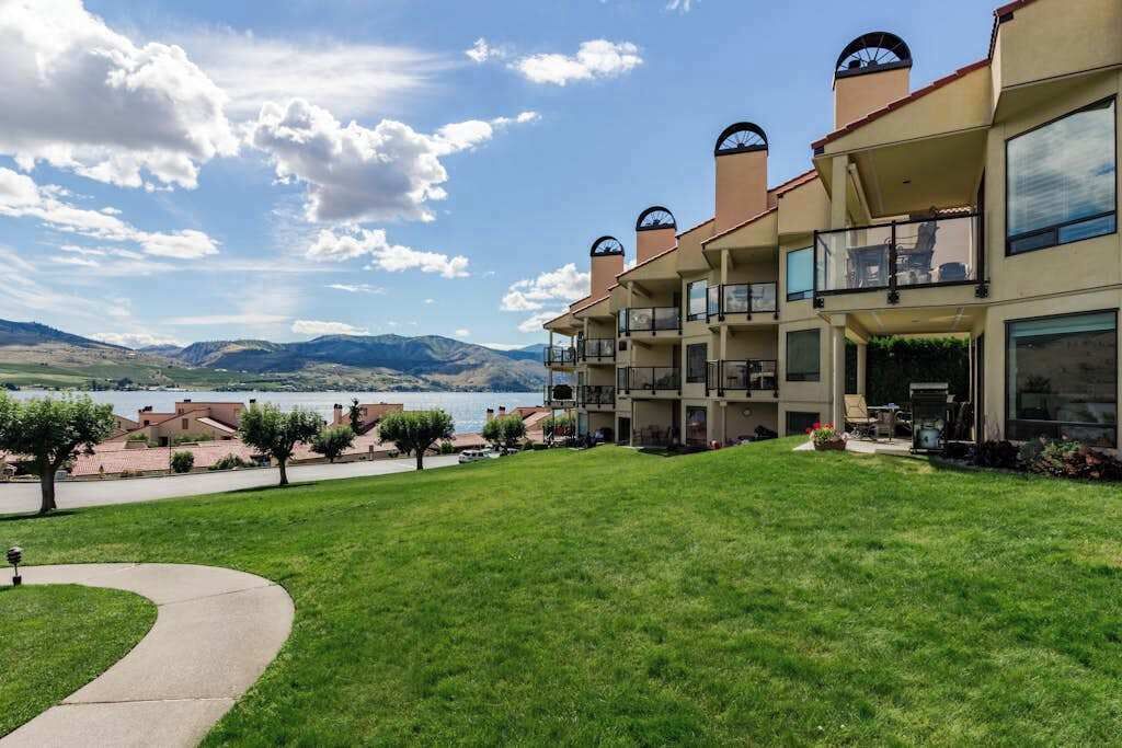 Ein mehrstöckiges Hotel mit Balkonen, einer Rasenfläche und Blick auf Berge und einen See.