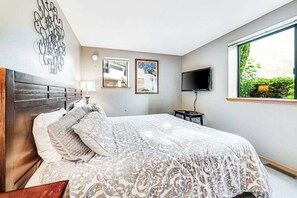 A bedroom with a large bed, a TV, a window, and artwork on the wall.