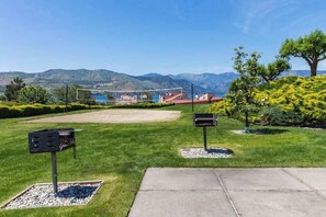 A well-maintained outdoor area with a paved walkway, a mailbox, and a grassy field with a mountain backdrop. - Luxe 2BR - Lakeview - Patio - Pool - Hot Tub (Chelan)