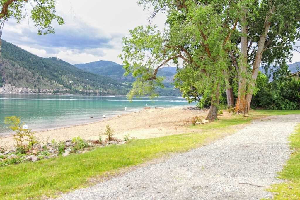 A gravel path leading to a beach with a lake and mountains in the background.