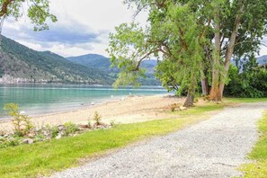 Ein Kiesweg führt zu einem Strand mit einem See und Bergen im Hintergrund.