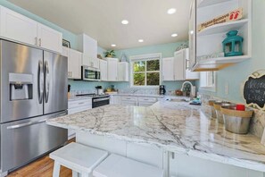 A modern kitchen with white cabinetry, a stainless steel refrigerator, a marble countertop, and a chalkboard with writing. - Hip 4BR Lakeview - Pool - Hot Tub - Deck (Manson)