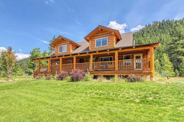 A two-story log cabin with a wrap-around porch and a large front deck.