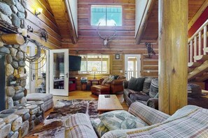 A log cabin interior with a stone wall, a ceiling with a deer skull, and a cozy seating area.