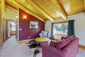 A room with a wooden ceiling, a red accent wall, a round coffee table, a purple sofa, and a cowhide rug. - 3BR mountain-view (Leavenworth)
