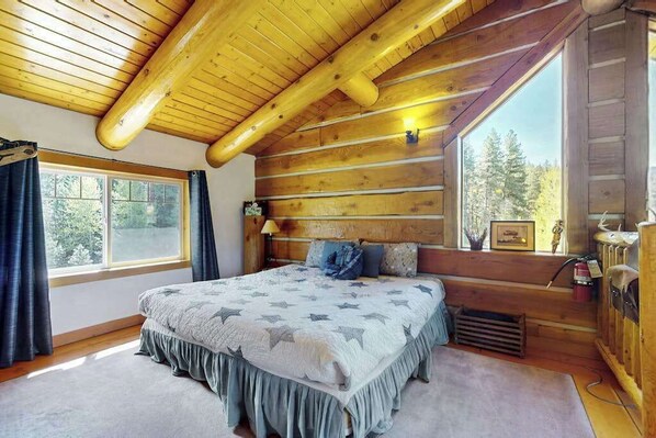A log cabin bedroom with a bed, a window, and a view of trees. - 3BR mountain-view (Leavenworth)