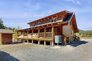 A wooden cabin with a porch, a small attached shed, and a gravel driveway.