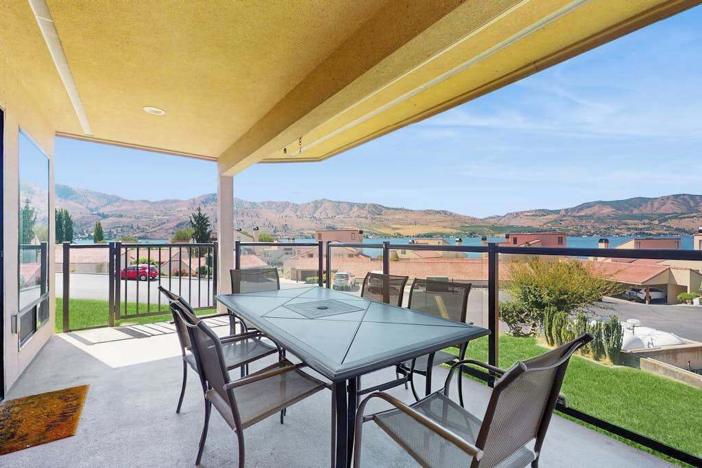 Une terrasse extérieure couverte, dotée d’une table et de chaises, qui offre une vue sur un quartier résidentiel et des collines.
