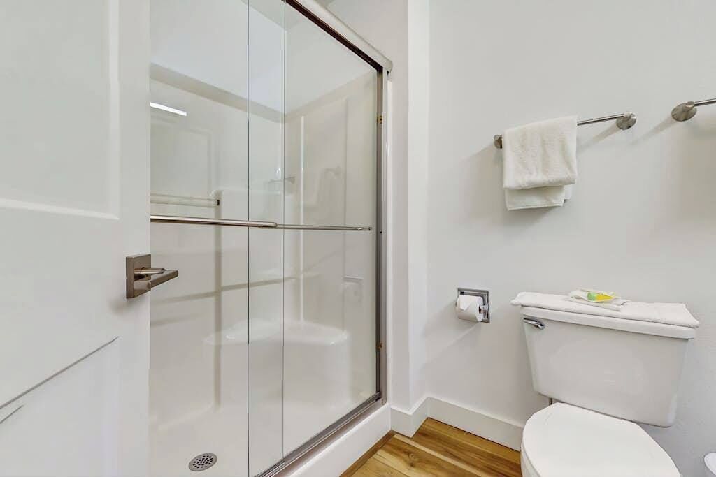 A bathroom with a glass shower enclosure, a toilet, and a towel rack.