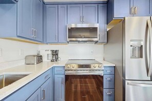 Eine Küche mit blauen Schränken, einer Edelstahl-Mikrowelle, einem Edelstahl-Kühlschrank und einem Kombi-Backofen.