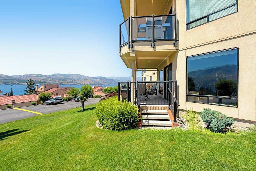 A modern two-story building with a balcony, a well-maintained lawn, and a view of the mountains.