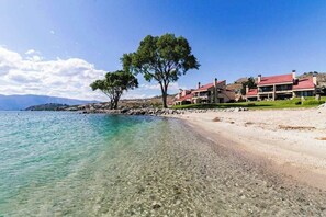 Ein Küsteneigentum mit einem klaren Strand, einem großen Baum und mehreren Gebäuden mit roten Dächern.