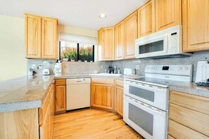 Eine moderne Küche mit Holzschränken, einer eingebauten Mikrowelle, einem Backofen mit Platz für zwei Auflaufformen und einem Geschirrspüler.