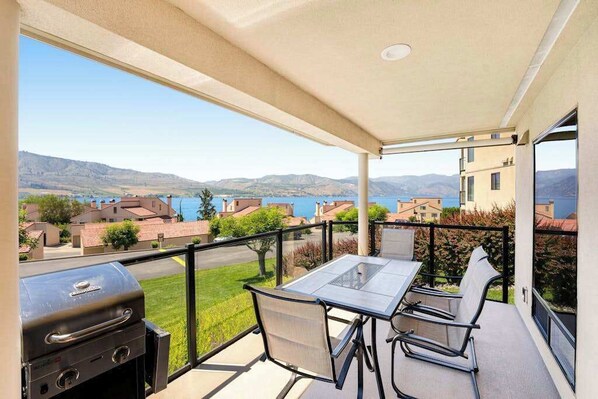 A balcony with a table and chairs, overlooking a residential area and a body of water. - 2BR Lakeview 1st-Floor - Deck - Pool (Chelan)