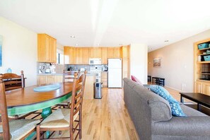 Eine moderne Küche mit Holzschränken, einem Esstisch und einem grauen Sofa in einem hellen Wohnbereich.
