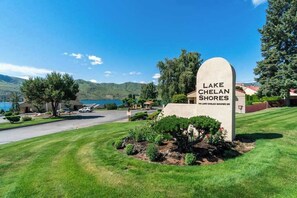 Schild für Lake Chelan Shores mit Blick auf eine Straße, Grünflächen und ferne Berge.