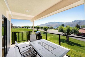A balcony with a table and chairs, overlooking a green landscape and mountains. - 2BR Lakeview 1st-Floor - Deck - Pool (Chelan)