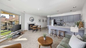A modern living room with a sofa, a coffee table, and a TV. There is a kitchen area with a microwave and a dining table. - Quiet 3BR Lakefront - Balcony - Pool (Chelan)