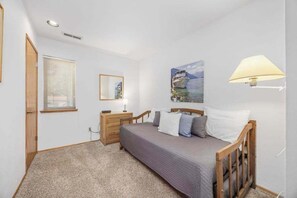 Un dormitorio con cama, mesita de noche, lámpara, ventana con persianas, un cuadro en la pared y una puerta.