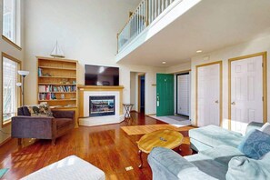 Ein geräumiges Wohnzimmer mit Kamin, Bücherregal und einer Treppe, die in einen oberen Bereich führt.