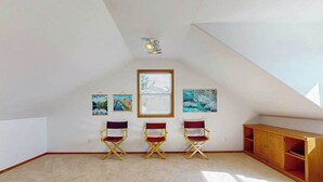 A room with a sloped ceiling, three fold-out chairs, a wooden cabinet, and three framed artworks on the wall. - Sunny 3BR Lakefront - Dock (Chelan)