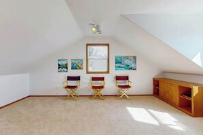 Ein Zimmer mit schrägem Dach, drei Klappstühlen, einer Holzkabine und drei gerahmten Kunstwerken an der Wand.