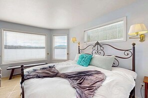 Ein Schlafzimmer mit einem Bett, zwei Nachttischlampen und zwei Fenstern mit Jalousien.