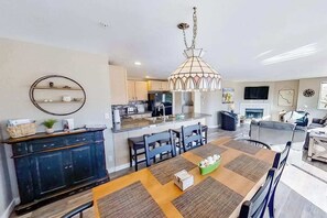 Une cuisine moderne dotée d’un îlot central, d’un coin repas avec une table et des chaises, et d’un espace de vie avec un canapé et une télévision.