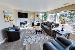 A living room with a fireplace, seating area, and large windows.