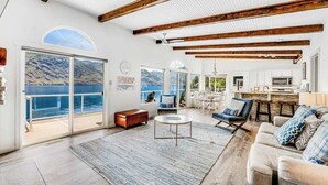 A spacious living area with a large window overlooking a body of water, wooden beams on the ceiling, and a cozy seating arrangement. - 4BR lakefront cottage & bunk house with dock (Chelan)