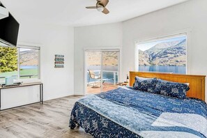 Une chambre avec un grand lit, un bureau et une vue sur un lac et des montagnes.