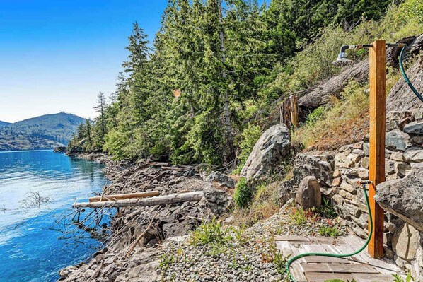 A natural landscape with a wooden deck, a stone wall, and a clear blue lake.