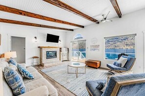 A living room with a fireplace, a large window with a view, and a ceiling fan.