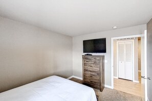 Ein Schlafzimmer mit einem Bett, einer Kommode, einem Fernseher und einer Tür zu einem anderen Raum.