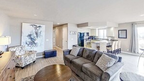 Een moderne woonkamer met een bank, fauteuil en salontafel. In de achtergrond is een keuken te zien.