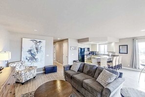 A modern living room with a sofa, armchair, and coffee table. There is a kitchen area visible in the background. - Exquisite 2BR Lakefront - Balcony - Pool (Chelan)