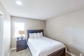 Un dormitorio con cama, mesita de noche, lámpara y ventana.