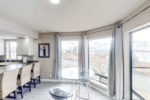 A modern kitchen with a bar area, large windows, and a view of a body of water. - Exquisite 2BR Lakefront - Balcony - Pool (Chelan)