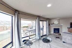 A spacious living area with large windows, a fireplace, and a clock on the wall. - Exquisite 2BR Lakefront - Balcony - Pool (Chelan)