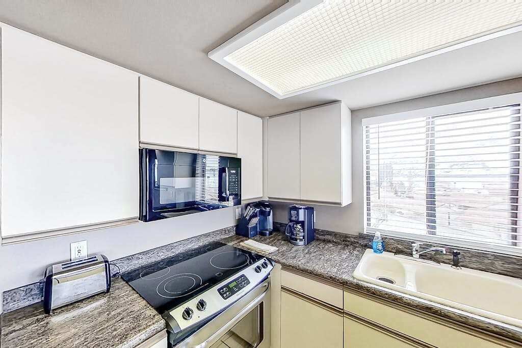 A kitchen with a microwave, stove, toaster, and a window with blinds.