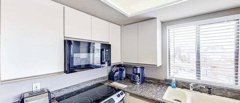 A kitchen with a microwave, stove, toaster, and a window with blinds.