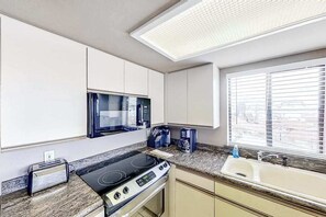 Eine Küche mit Mikrowelle, Herd, Toaster und einem Fenster mit Jalousien.