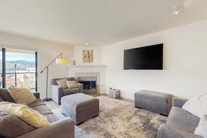 Ein modernes Wohnzimmer mit Kamin, grauen Sofas und einem großen Fernseher an der Wand.