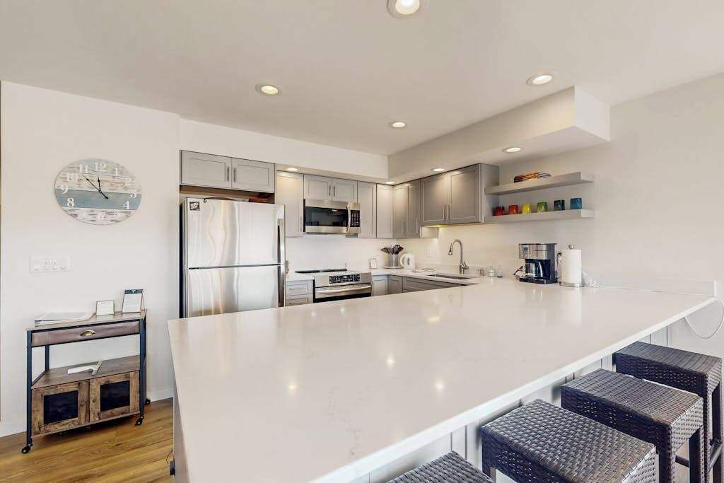 A modern kitchen with a large island, stainless steel appliances, and a clock on the wall.
